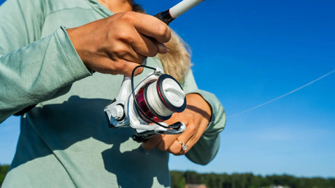 Person holding Max Pro Spinning Rod And Reel Combo 6 Foot 10 Inch, Size 2500 Reel, open in hands against a blue sky background.