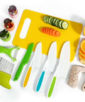 Melican 11-piece kids kitchen knife set on yellow cutting board with colorful handles, peeler, cucumber and oranges.