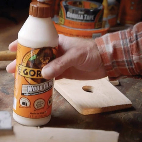 Hand holding Wood Glue For Indoor And Outdoor Projects, 18 Ounce Bottle, Natural Color, 2 Pack, Quick Clamp Time, on wooden table.