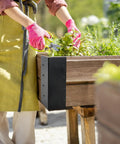 Person using 8 Pack Kickass Metal Corner Brackets For Raised Garden Beds 3X3X6 Inch to cut herbs in a wooden planter.