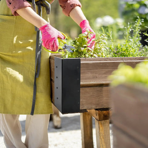 Person using 8 Pack Kickass Metal Corner Brackets For Raised Garden Beds 3X3X6 Inch to cut herbs in a wooden planter.