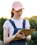 Woman wearing Omnia Vincit Pink Breathable Hat For Women With Adjustable Buckle Everyday Wear Cap outdoors writing in notebook
