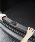 Spigen rear bumper trunk sill guard, black, for 2025/2026 Tesla Model Y; hands hold the edge.