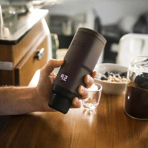 Portable Espresso Maker For Ground Coffee And NS Capsules, 20 Bar Pressure, dark burgundy, shown in hand on table.