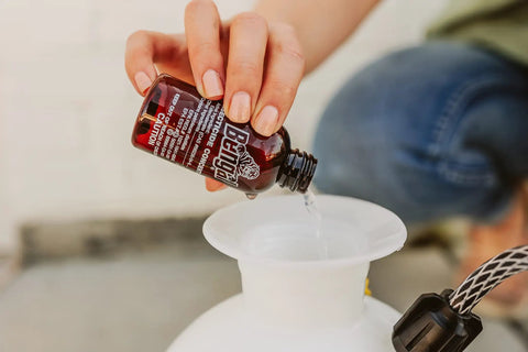 Pouring Indoor Outdoor Bug Killer Concentrate Makes 2 Gallons From 2 Oz Liquid into a sprayer for pest control