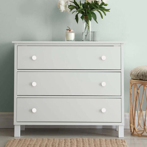 Modern white dresser with three drawers and round white cabinet knobs, styled with flowers and a candle.