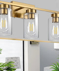 Clean Three Light Bathroom Vanity Wall Sconce In Smooth Brushed Gold Finish With Clear Retro Glass Shades, above mirror setup.