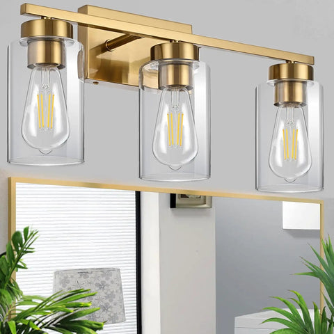Clean Three Light Bathroom Vanity Wall Sconce In Smooth Brushed Gold Finish With Clear Retro Glass Shades, above mirror setup.