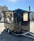 Slick 12 Foot Black Stainless Steel Commercial Food Trailer Equipped With Turnkey Mobile Beer Bar Station And Tough Catering Gear For A No Fuss Pop Up Hustle, angled view in plaza.