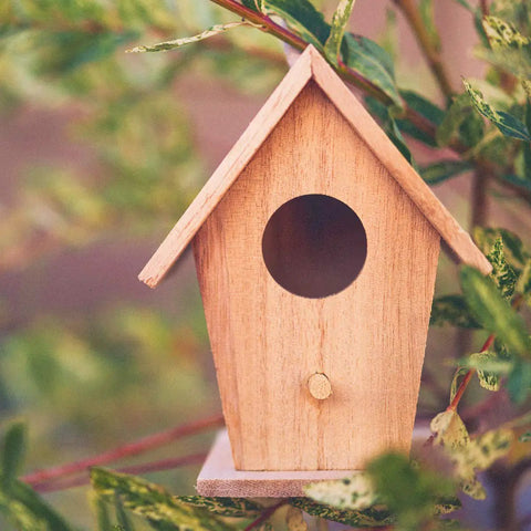 Wooden birdhouse nestled in green foliage, showcasing a circular entrance and pointed roof design.