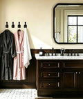 Top Shelf Matte Black Wall Coat Hooks Four Pack holding bathrobes in a stylish bathroom setting with a modern sink.