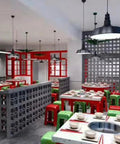 Restaurant interior with colorful square tables, red and green stools, and decorative concrete block walls under industrial lights.