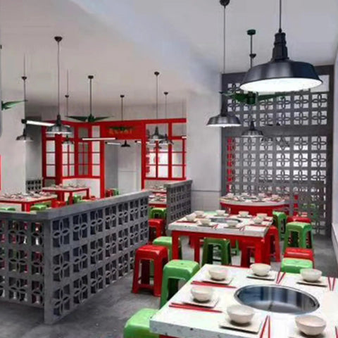 Restaurant interior with colorful square tables, red and green stools, and decorative concrete block walls under industrial lights.