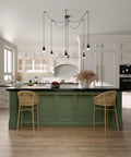 Modern kitchen with green island, wicker bar stools, hanging pendant lights, and white cabinets; neutral decor style.