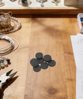 Round Graphite Electrode Plates For Melting And Electrolysis 10 Pieces on a workshop table with jewelry tools