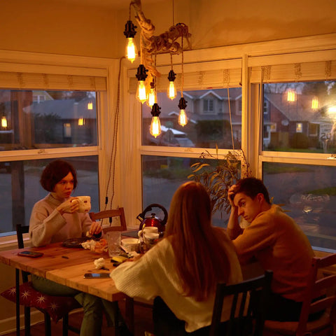 People sitting at a wooden table under warm hanging lights in a dining room during sunset.