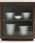 Wooden cabinet with fluted glass door showcasing white cups and bowls inside, metal handle, antique design