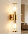 Klighten Hardwired Wall Sconce Modern Brushed Brass Bathroom Vanity Light on a wall with glass rods diffusing warm light.