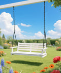 White wooden porch swing with black chains in a garden with colorful flowers under a blue sky with clouds.