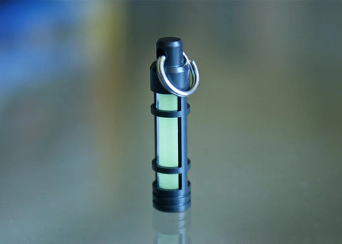 Embrite Glow Fob With Green Embrite Pellet, Aircraft-Grade Aluminum Keychain Accessory standing on reflective surface