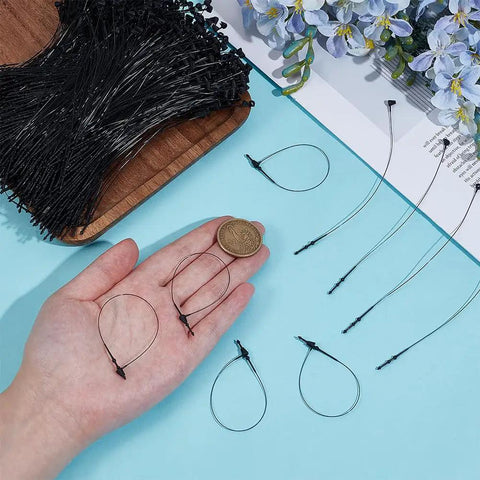 2000 Pack 5 Inch Black Plastic Hang Tag Loops Featuring Straight Up Secure Snap Lock Fasteners in hand with coin for size.