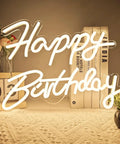 Lit Adjustable Dimmable Happy Birthday Neon Sign LED Light Up Backdrop For Parties on tabletop with books and flowers.