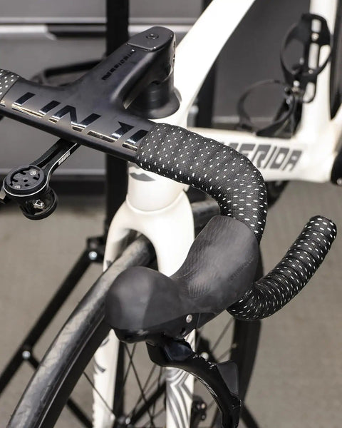 Road Bike Handlebar Tape With Silicone Surface on black taped handlebars on white bike focusing on grip and aluminum plugs.