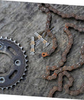 Rusty metal chain and gear with bolts on textured surface, viewed from above