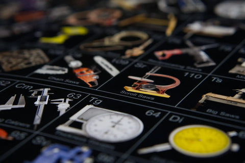Close-up of Periodic Table Of Tools Poster showing various hand tools, including calipers and saws, on dark glossy paper.