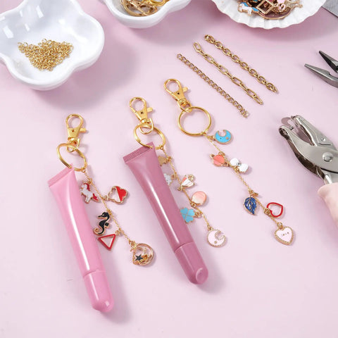 All In One Lip Gloss Keychain Making Kit With 100 Enamel Charms, Clips, Chains, Pliers, Hole Punch And Gift Bags arranged on table.