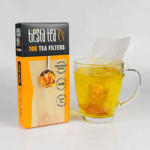 Box of Disposable Loose Leaf Tea Filters For Easy Brewing with glass cup of tea, unbleached paper sachet visible, 100 empty bags.