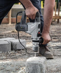 Electric SDS-Plus Rotary Demolition Hammer 1180W with 1-1/4 inch bit in use on concrete block outdoors