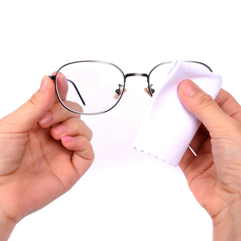 Eyeglasses with metal frame being wiped by white microfiber cloth