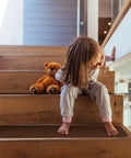 Child sitting on wooden stairs with a teddy bear, showcasing Set Of 15 Skid Resistant Carpet Stair Treads In Chocolate Brown 8 Inch By 27 Inch.