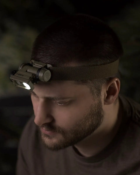 Person wearing Sidewinder 55 Lumen Compact II Military Flashlight with helmet mount in coyote finish, providing hands-free lighting.