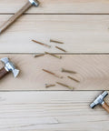 Scattered nails and wooden hammers on a wooden surface, representing tools for 100 Piece M6 Zinc Plated Furniture Bolts And Nuts Kit.