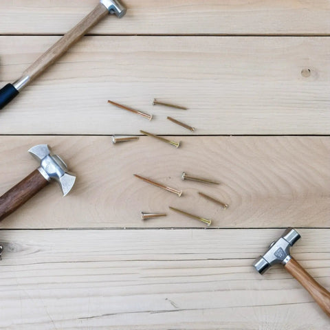 Scattered nails and wooden hammers on a wooden surface, representing tools for 100 Piece M6 Zinc Plated Furniture Bolts And Nuts Kit.