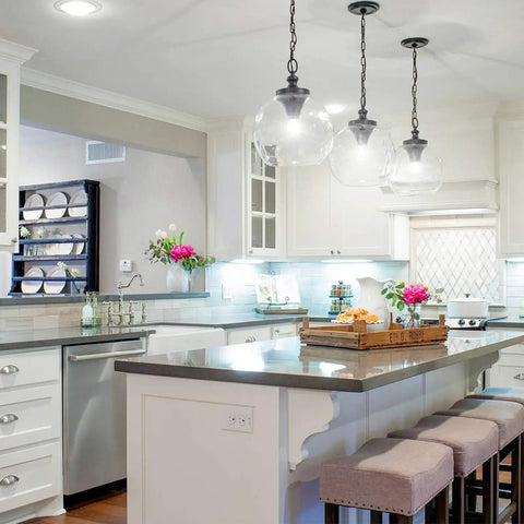 Modern kitchen with pendant lighting, featuring a tray with flowers and decor on a central island, stools, and white cabinetry.