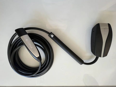 Tesla EV charging cable with black sheath and silver accent handle, coiled on white surface