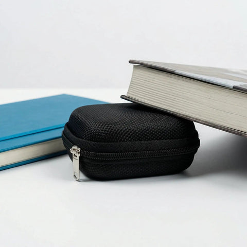 Hearing Aid Case With Travel Pouch And Battery Holder next to books, showcasing compact black EVA shell, waterproof storage.