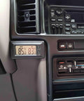 Black dual-display digital car thermometer mounted on the dashboard near the vent, showing outside and inside temperatures in Fahrenheit.