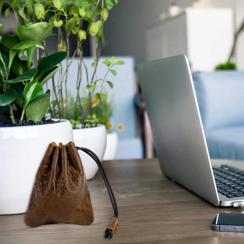 Hardy Cowhide Leather Drawstring Pouch With Vintage Retro Finish Designed For Hauling Your Daily Grind Essentials Travel Toiletries And Quick Pocket Stash next to a laptop on a table.