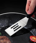 Small stainless steel slotted spatula with black handle, close-up in frying pan.