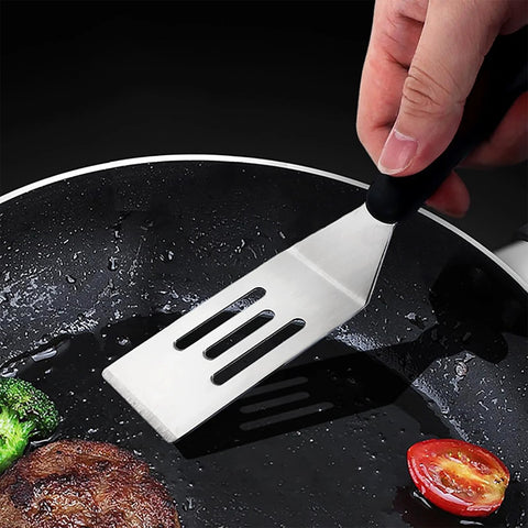 Small stainless steel slotted spatula with black handle, close-up in frying pan.