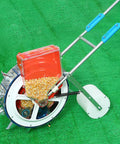 Walk Behind Garden Seeder With 16 Outlets For Easy No Fuss Planting, showing corn seeds in hopper, on green grass