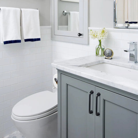 Modern bathroom with gray vanity, white countertop, and silver faucet beside white toilet and tiled wall.