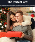 Smiling couple exchanging a wrapped gift in a festive decorated living room with Christmas tree and lights.