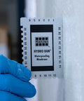 Laticrete Hydro Ban waterproofing membrane being measured with gauge tool on a white wall, showcasing application process.