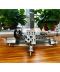 Compact Mini Metal Lathe For Benchtop Use With 3 Jaw Chuck And Tailstock on wooden surface with plants in background.