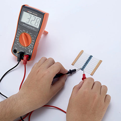 Front view of orange digital multimeter with red/black probes testing a row of blue axial resistors on a strip.